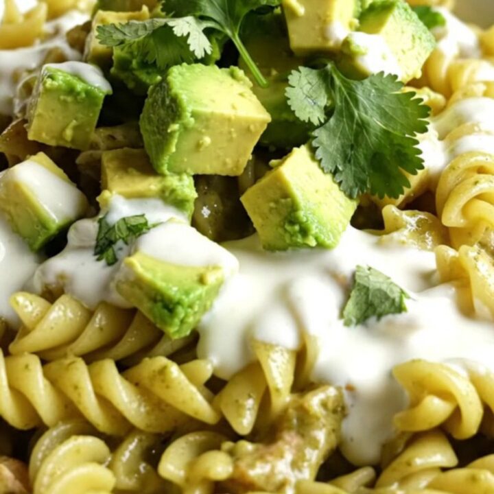 A vibrant bowl of creamy green chili chicken pasta topped with fresh avocado, crema, and cilantro.