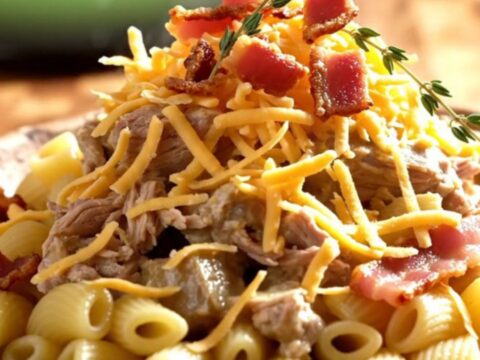 A steaming scoop of creamy white cheddar pasta with tender pork, maple bacon, and apples in a forest-green slow cooker.