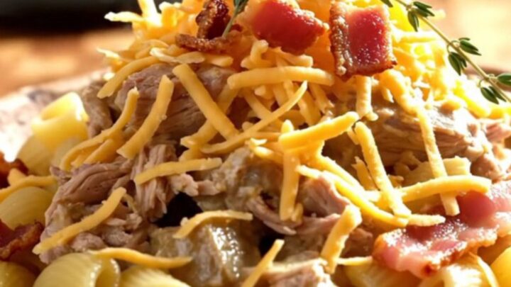 A steaming scoop of creamy white cheddar pasta with tender pork, maple bacon, and apples in a forest-green slow cooker.
