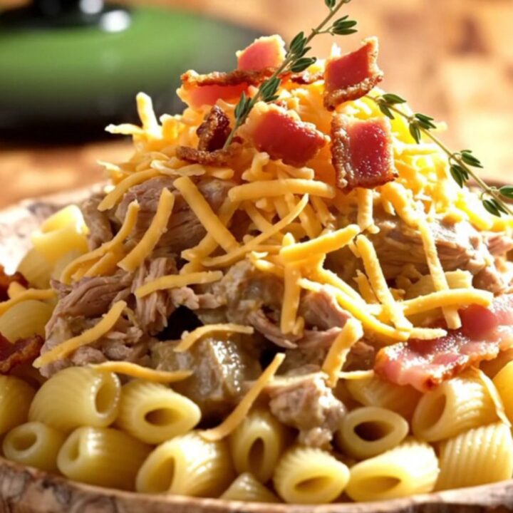 A steaming scoop of creamy white cheddar pasta with tender pork, maple bacon, and apples in a forest-green slow cooker.