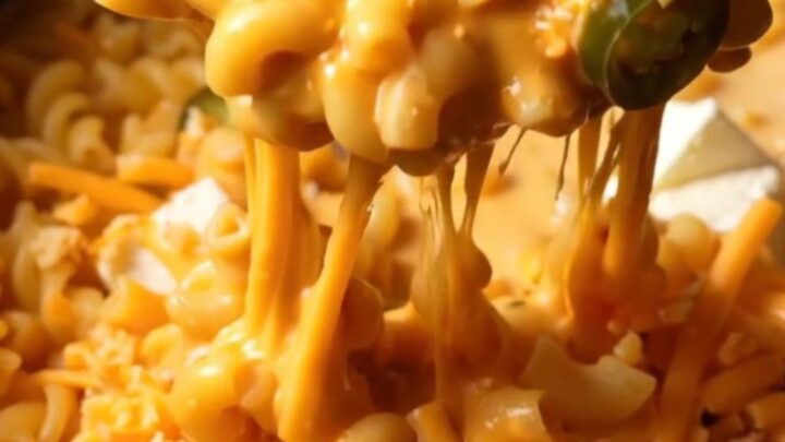 A close-up shot of creamy jalapeno popper mac and cheese in a crockpot, topped with crispy bacon and charred jalapenos.
