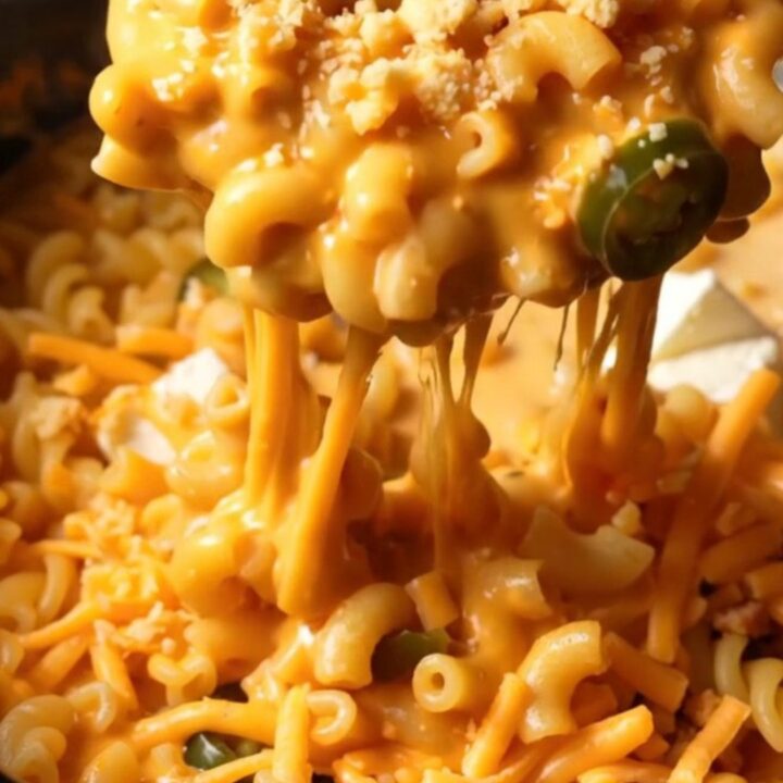 A close-up shot of creamy jalapeno popper mac and cheese in a crockpot, topped with crispy bacon and charred jalapenos.