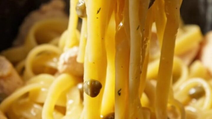 Close-up of creamy chicken piccata pasta with capers and lemon slices in a bright setting.