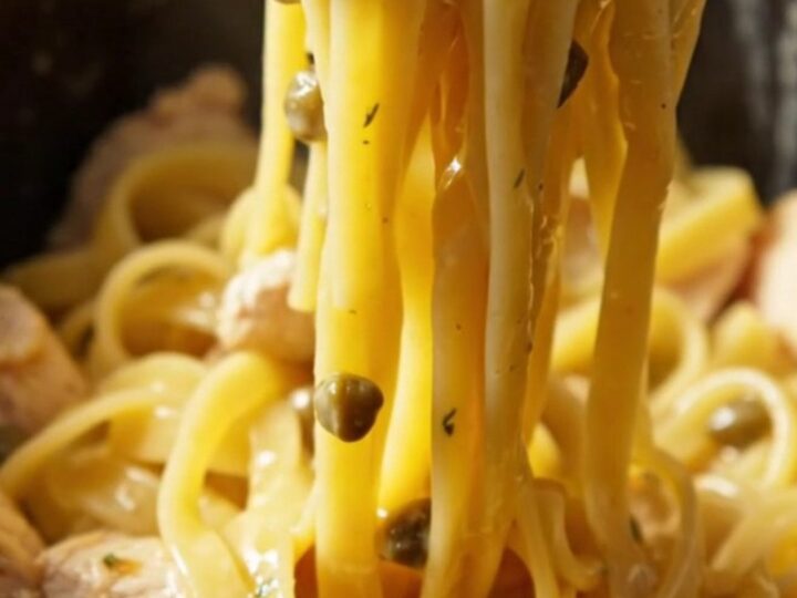 Close-up of creamy chicken piccata pasta with capers and lemon slices in a bright setting.