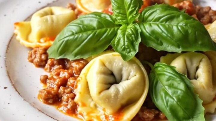 A close-up of a bubbling slow-cooker tortellini Bolognese bake topped with golden, melted mozzarella and fresh basil.