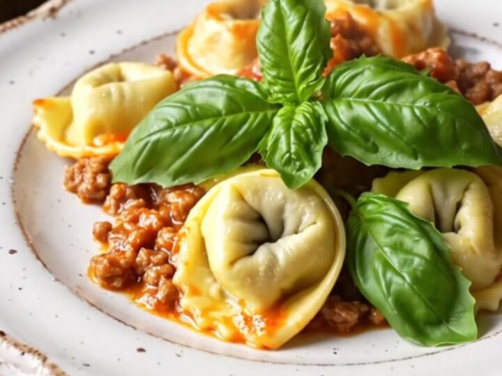 A close-up of a bubbling slow-cooker tortellini Bolognese bake topped with golden, melted mozzarella and fresh basil.