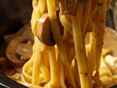A close-up of creamy chicken Marsala fettuccine with mushrooms in a rustic bowl.