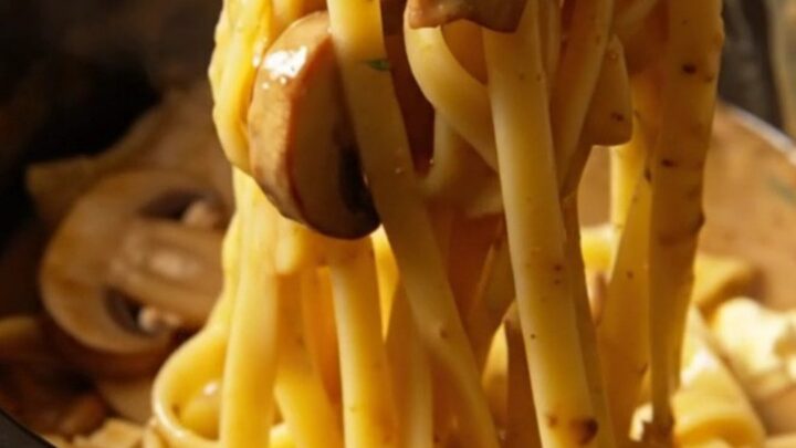 A close-up of creamy chicken Marsala fettuccine with mushrooms in a rustic bowl.