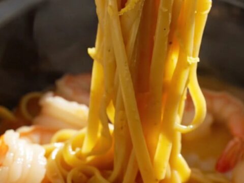 A close-up of creamy saffron linguine with jumbo shrimp and bay scallops in a blue ceramic slow cooker.