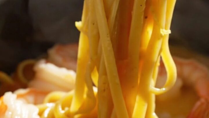 A close-up of creamy saffron linguine with jumbo shrimp and bay scallops in a blue ceramic slow cooker.