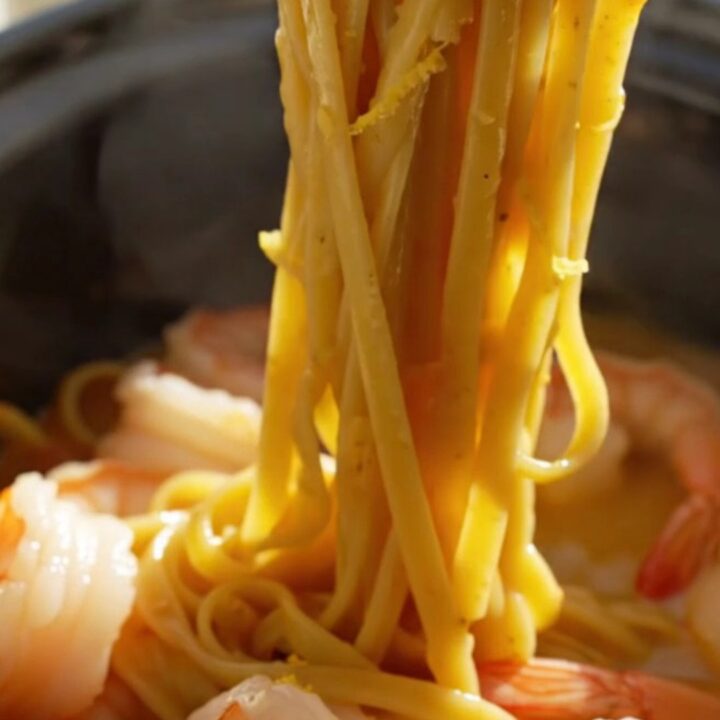 A close-up of creamy saffron linguine with jumbo shrimp and bay scallops in a blue ceramic slow cooker.