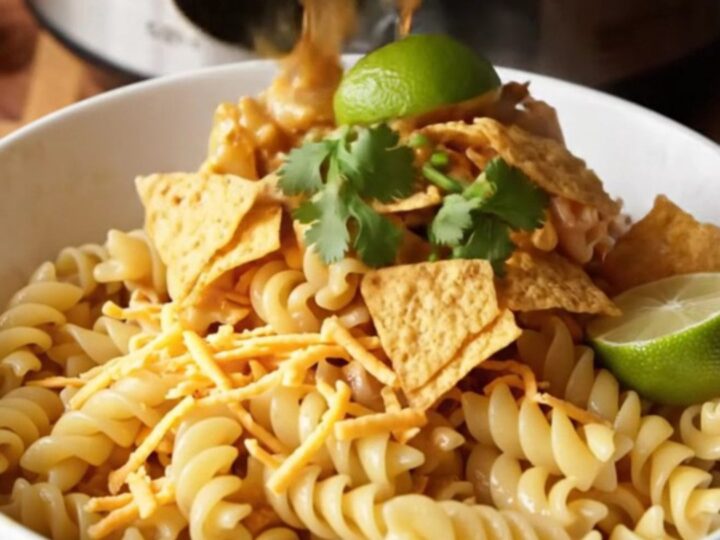 A steaming bowl of southwest chicken pasta topped with crushed tortilla chips, cilantro, and a lime wedge.
