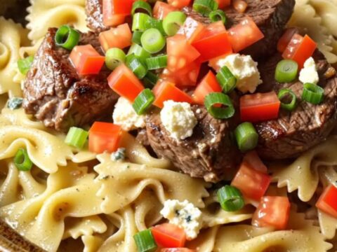 A close-up of blackened steak and farfalle pasta in a creamy blue cheese sauce served in a ceramic bowl.