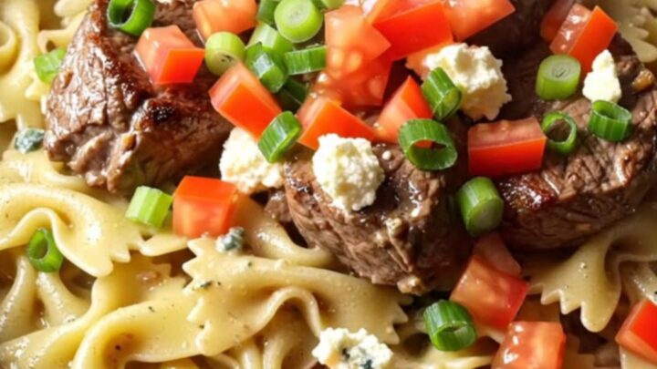 A close-up of blackened steak and farfalle pasta in a creamy blue cheese sauce served in a ceramic bowl.