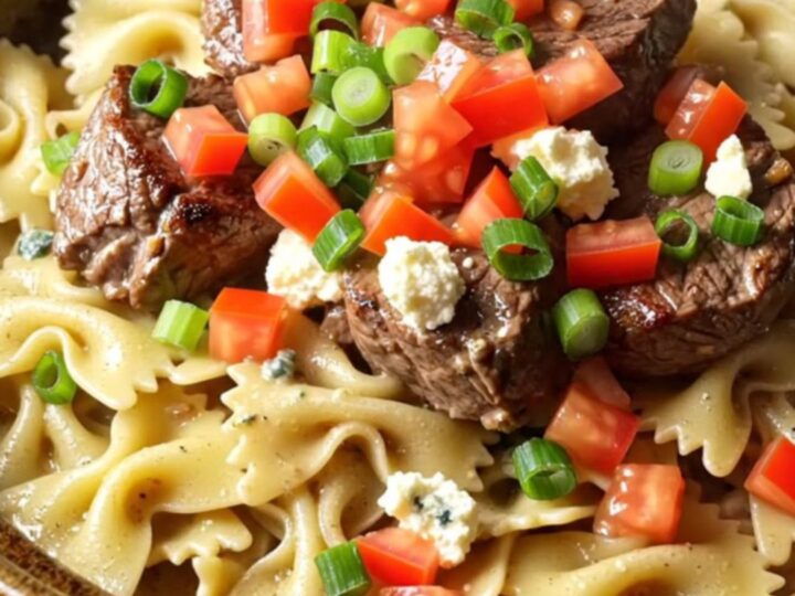 A close-up of blackened steak and farfalle pasta in a creamy blue cheese sauce served in a ceramic bowl.