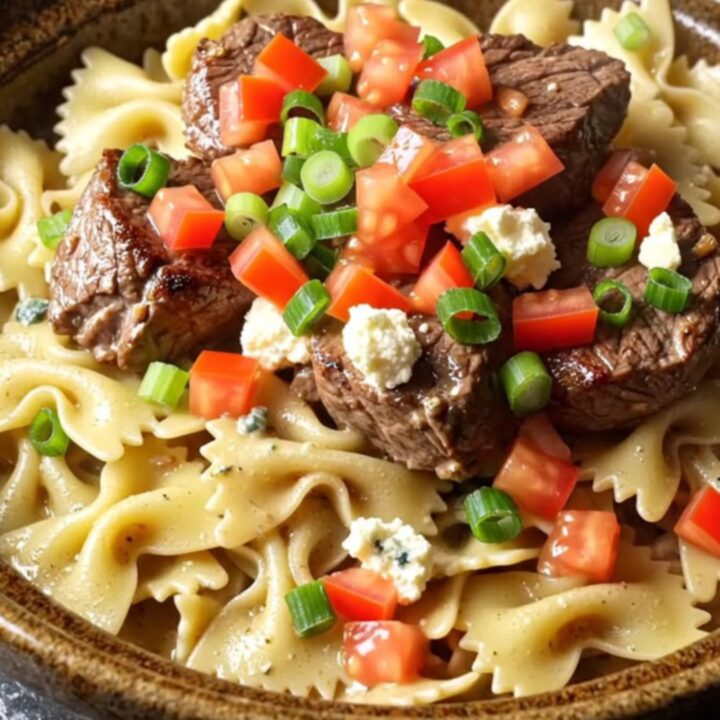 A close-up of blackened steak and farfalle pasta in a creamy blue cheese sauce served in a ceramic bowl.