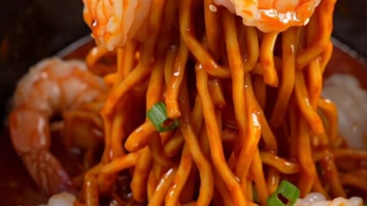 A close-up of glossy spaghetti noodles tossed with jumbo shrimp and a vibrant red chili crisp garlic butter sauce.