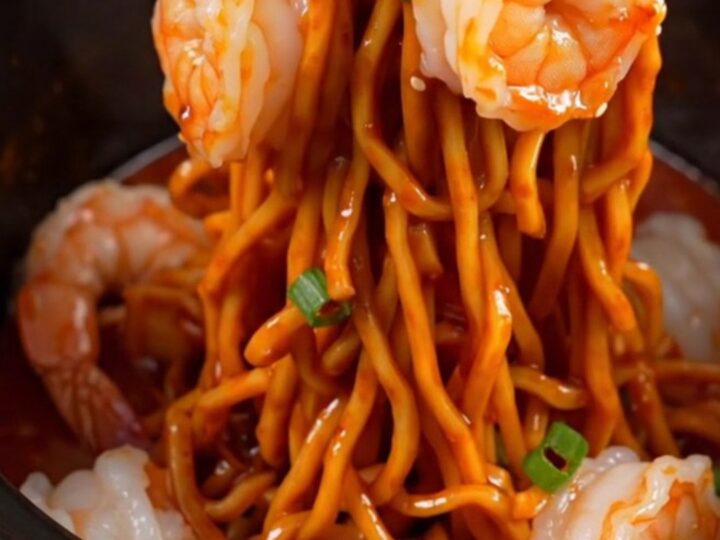 A close-up of glossy spaghetti noodles tossed with jumbo shrimp and a vibrant red chili crisp garlic butter sauce.