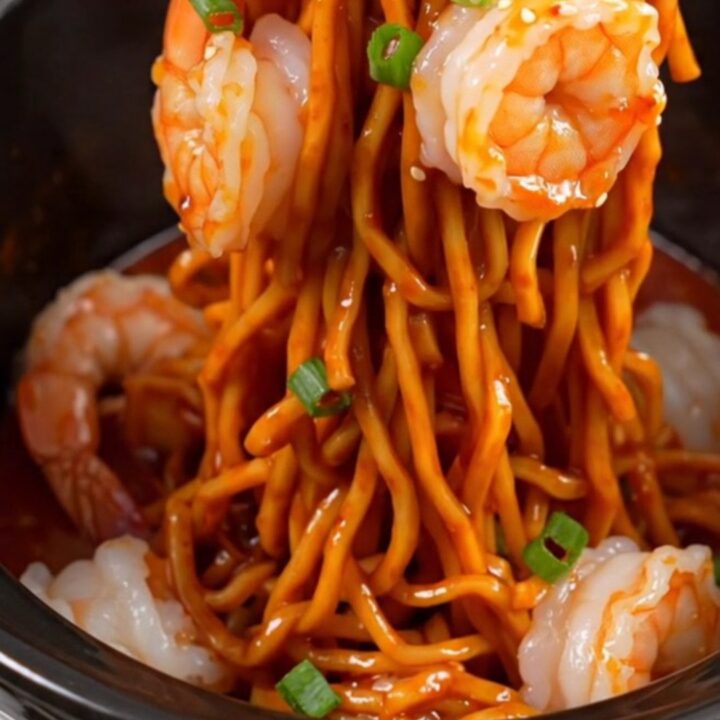 A close-up of glossy spaghetti noodles tossed with jumbo shrimp and a vibrant red chili crisp garlic butter sauce.