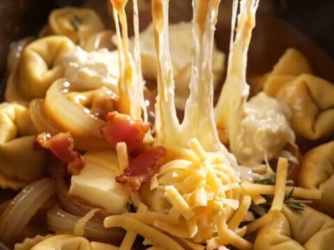 A steaming bowl of French onion tortellini topped with melted Gruyere and crispy bacon bits.