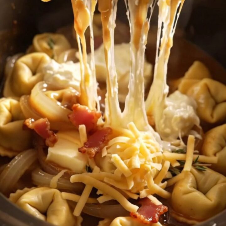 A steaming bowl of French onion tortellini topped with melted Gruyere and crispy bacon bits.