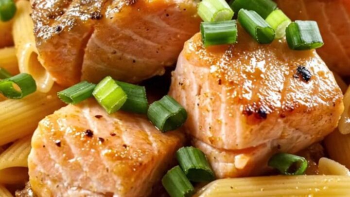 A close-up view of creamy Cajun honey-butter salmon pasta topped with charred lemon wheels.