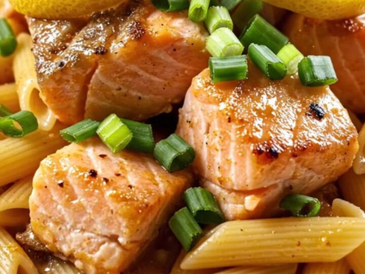 A close-up view of creamy Cajun honey-butter salmon pasta topped with charred lemon wheels.