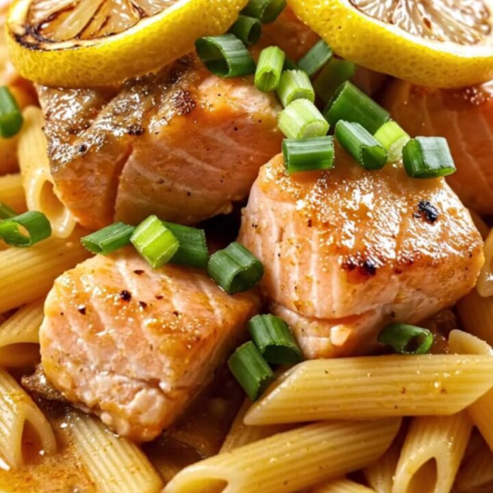 A close-up view of creamy Cajun honey-butter salmon pasta topped with charred lemon wheels.