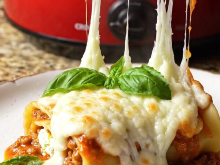 A close-up shot of spinach and ricotta lasagna roll-ups in a Crockpot with melted mozzarella.