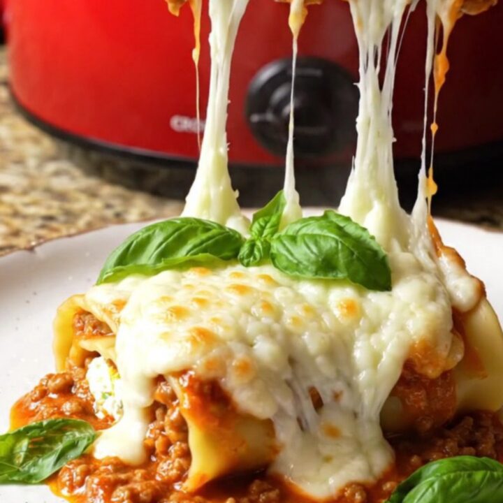 A close-up shot of spinach and ricotta lasagna roll-ups in a Crockpot with melted mozzarella.