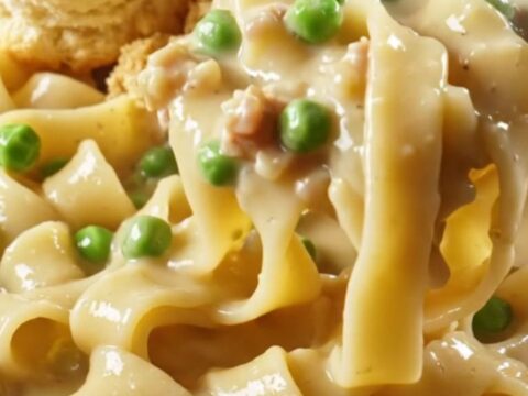 A steaming bowl of creamy chicken pot pie noodles topped with golden biscuit crumbles and fresh parsley.