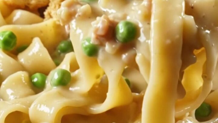A steaming bowl of creamy chicken pot pie noodles topped with golden biscuit crumbles and fresh parsley.
