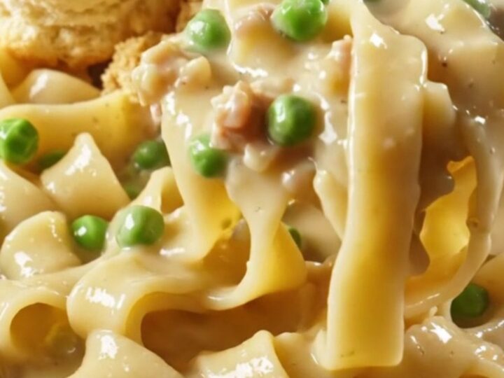 A steaming bowl of creamy chicken pot pie noodles topped with golden biscuit crumbles and fresh parsley.