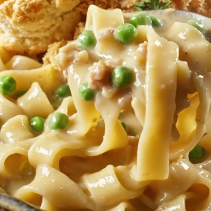 A steaming bowl of creamy chicken pot pie noodles topped with golden biscuit crumbles and fresh parsley.