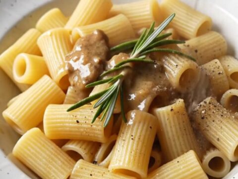 A close-up of steakhouse beef tips and rigatoni in a creamy sauce garnished with fresh rosemary.