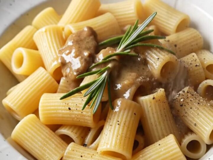 A close-up of steakhouse beef tips and rigatoni in a creamy sauce garnished with fresh rosemary.