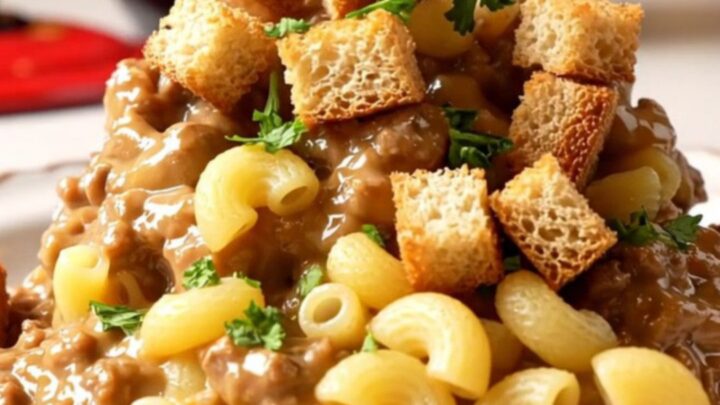 A close-up of a bowl of creamy patty melt mac and cheese topped with toasted rye croutons and fresh parsley.