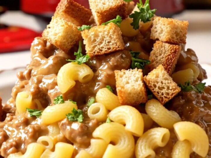 A close-up of a bowl of creamy patty melt mac and cheese topped with toasted rye croutons and fresh parsley.