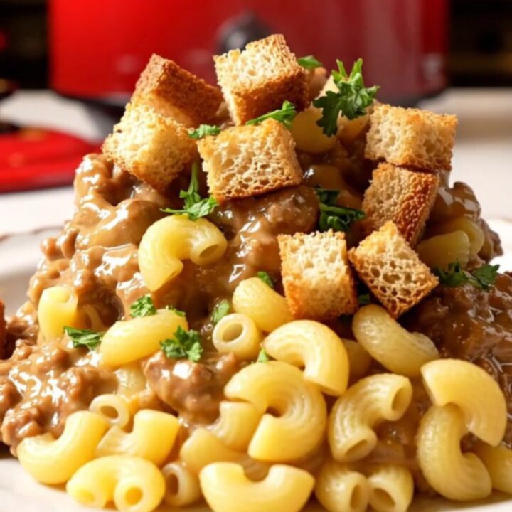 A close-up of a bowl of creamy patty melt mac and cheese topped with toasted rye croutons and fresh parsley.