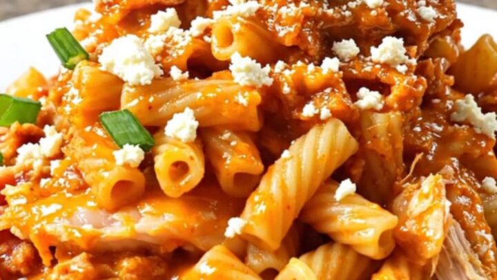 A steaming bowl of creamy buffalo chicken pasta topped with bacon, blue cheese, and green onions.