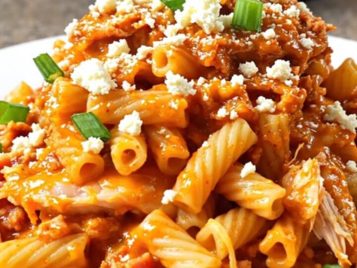 A steaming bowl of creamy buffalo chicken pasta topped with bacon, blue cheese, and green onions.