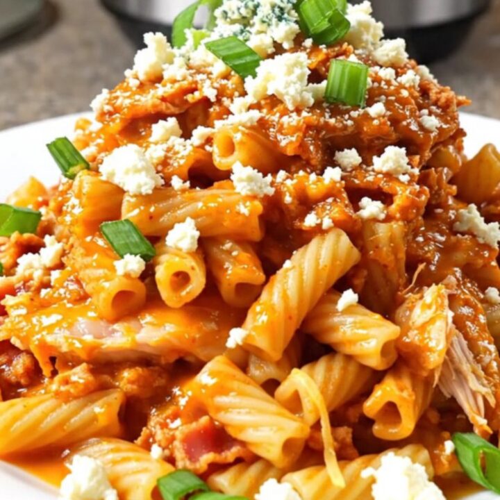 A steaming bowl of creamy buffalo chicken pasta topped with bacon, blue cheese, and green onions.