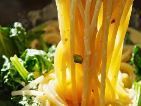 Close-up of spaghetti coated in a creamy lemon ricotta sauce with pistachios and spinach in a white crockpot.