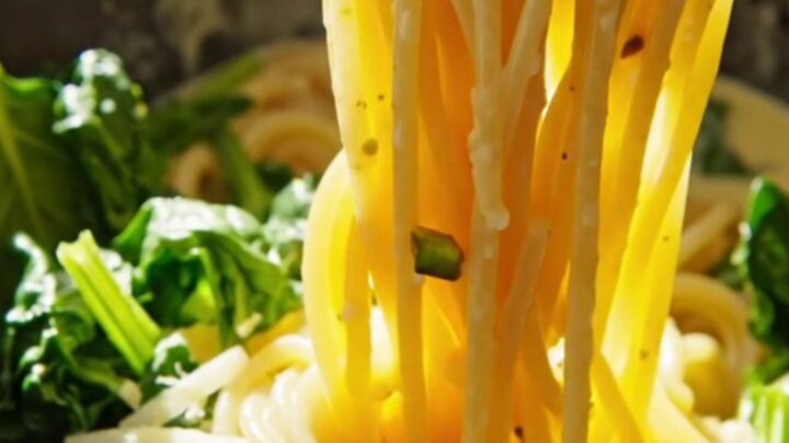 Close-up of spaghetti coated in a creamy lemon ricotta sauce with pistachios and spinach in a white crockpot.