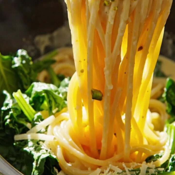 Close-up of spaghetti coated in a creamy lemon ricotta sauce with pistachios and spinach in a white crockpot.