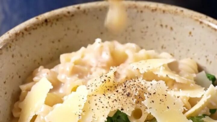 A glossy navy-blue Crockpot with the lid lifted, revealing creamy Italian wedding soup with meatballs and pasta.