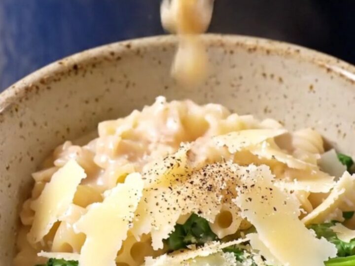 A glossy navy-blue Crockpot with the lid lifted, revealing creamy Italian wedding soup with meatballs and pasta.