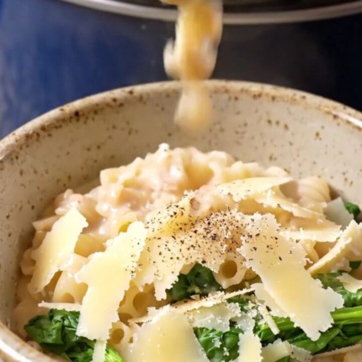 A glossy navy-blue Crockpot with the lid lifted, revealing creamy Italian wedding soup with meatballs and pasta.