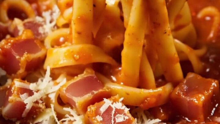 A close-up of bucatini pasta in a glossy tomato sauce with crispy guanciale pieces and grated pecorino cheese.