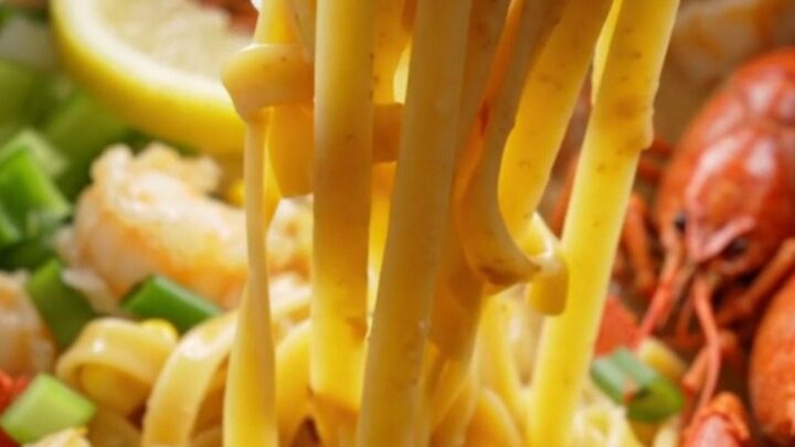 A close-up of creamy crawfish etouffee fettuccine served in a bowl, topped with green onions and lemon wedges.